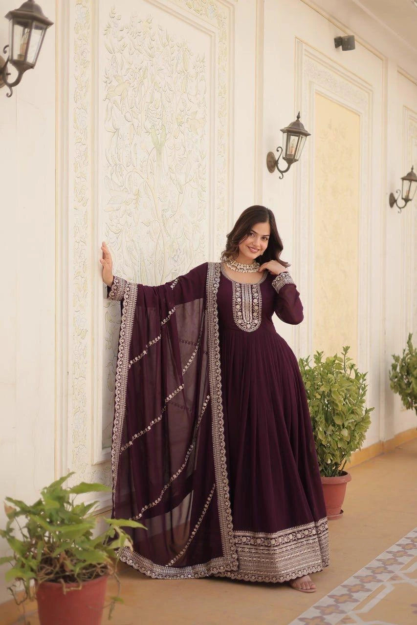 Woman in a dark purple traditional outfit with silver embroidery standing in a decorated room.