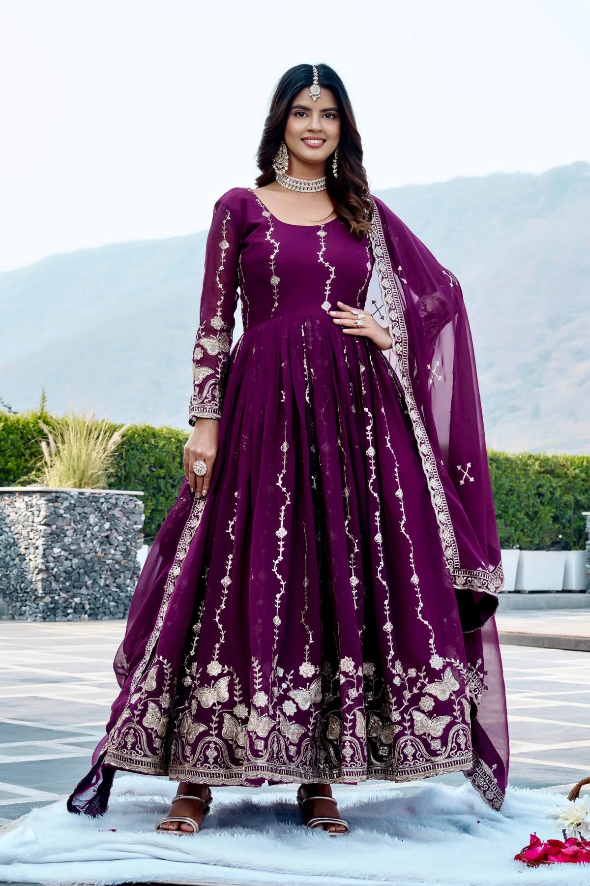 Woman in a purple traditional outfit with white patterns standing outdoors.