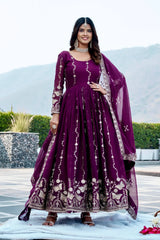 Woman in a purple traditional outfit with white patterns standing outdoors.