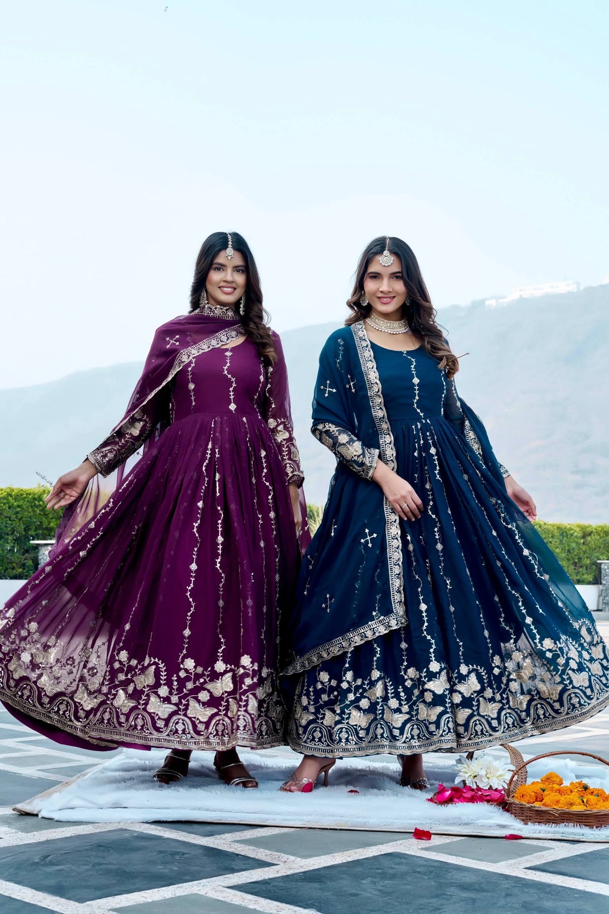Two women in traditional embroidered dresses standing outdoors with a scenic background.