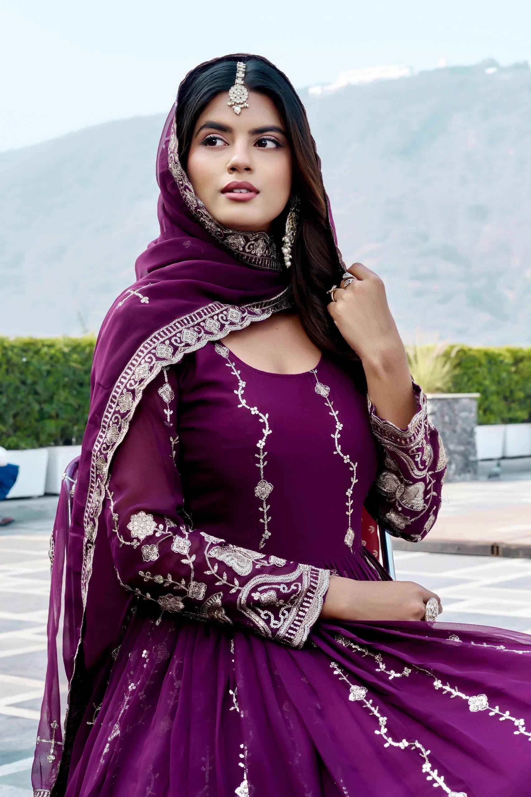 Woman in a purple traditional outfit with intricate designs outdoors.