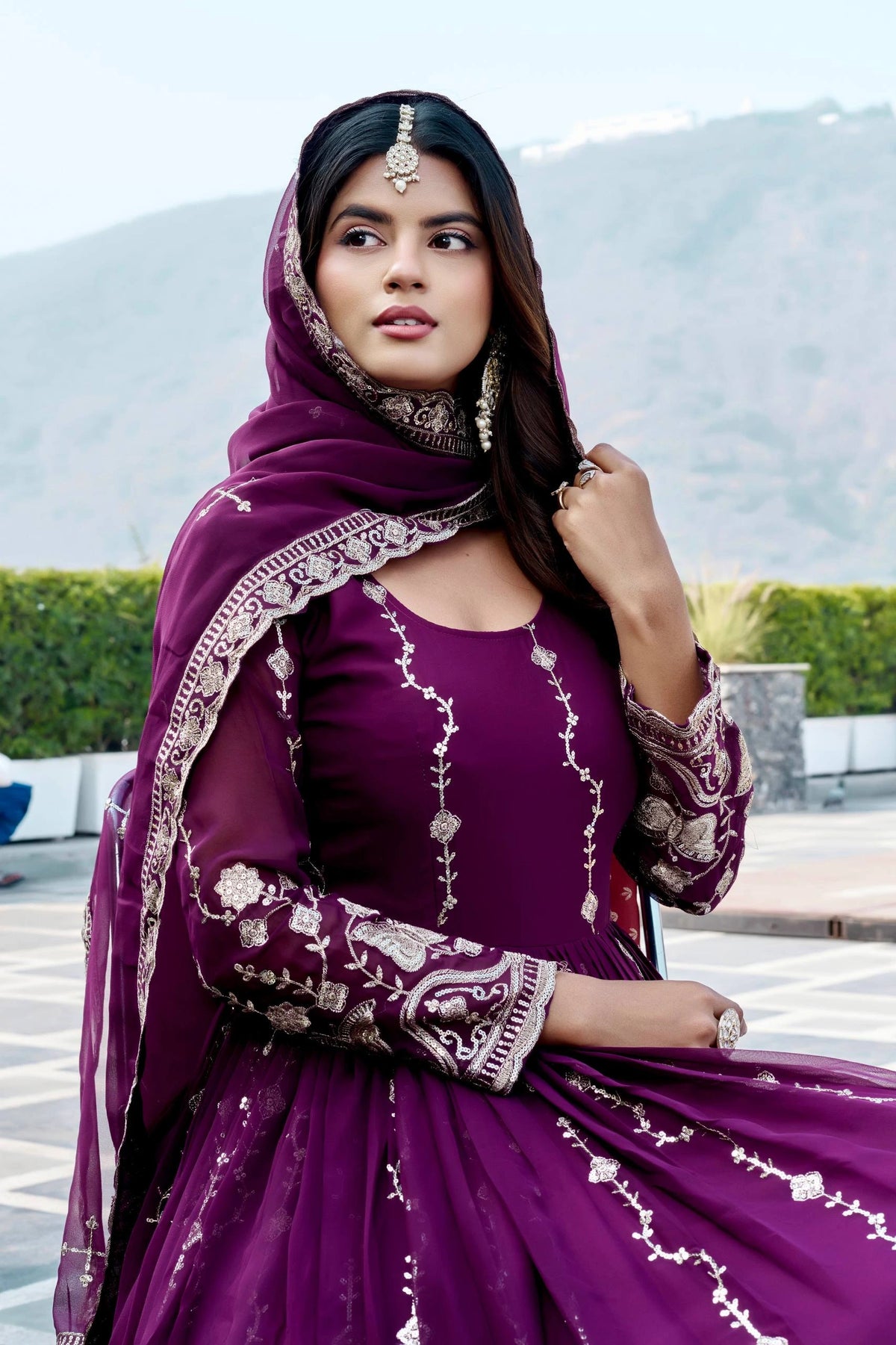 Woman in a purple traditional outfit with intricate designs outdoors.