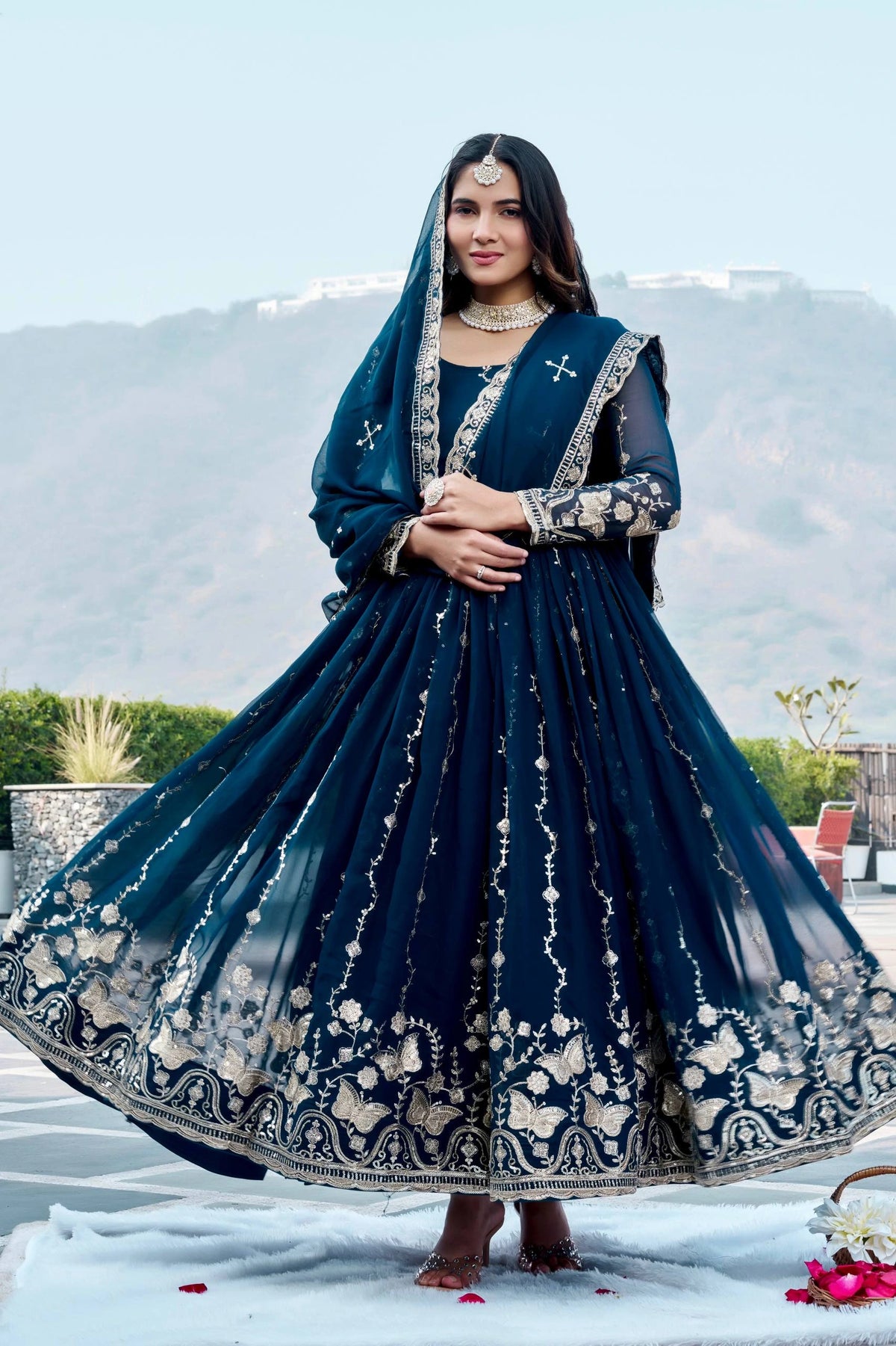 Woman in a traditional blue embroidered outfit with a scenic background