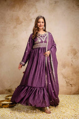 Woman wearing a purple embroidered dress against a textured beige wall.