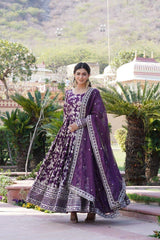 Woman in a purple traditional outfit standing outdoors with greenery and architecture in the background