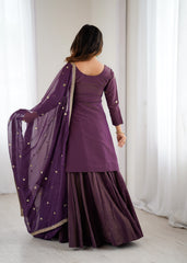 Woman wearing a purple traditional outfit with a sheer dupatta against a white curtain background