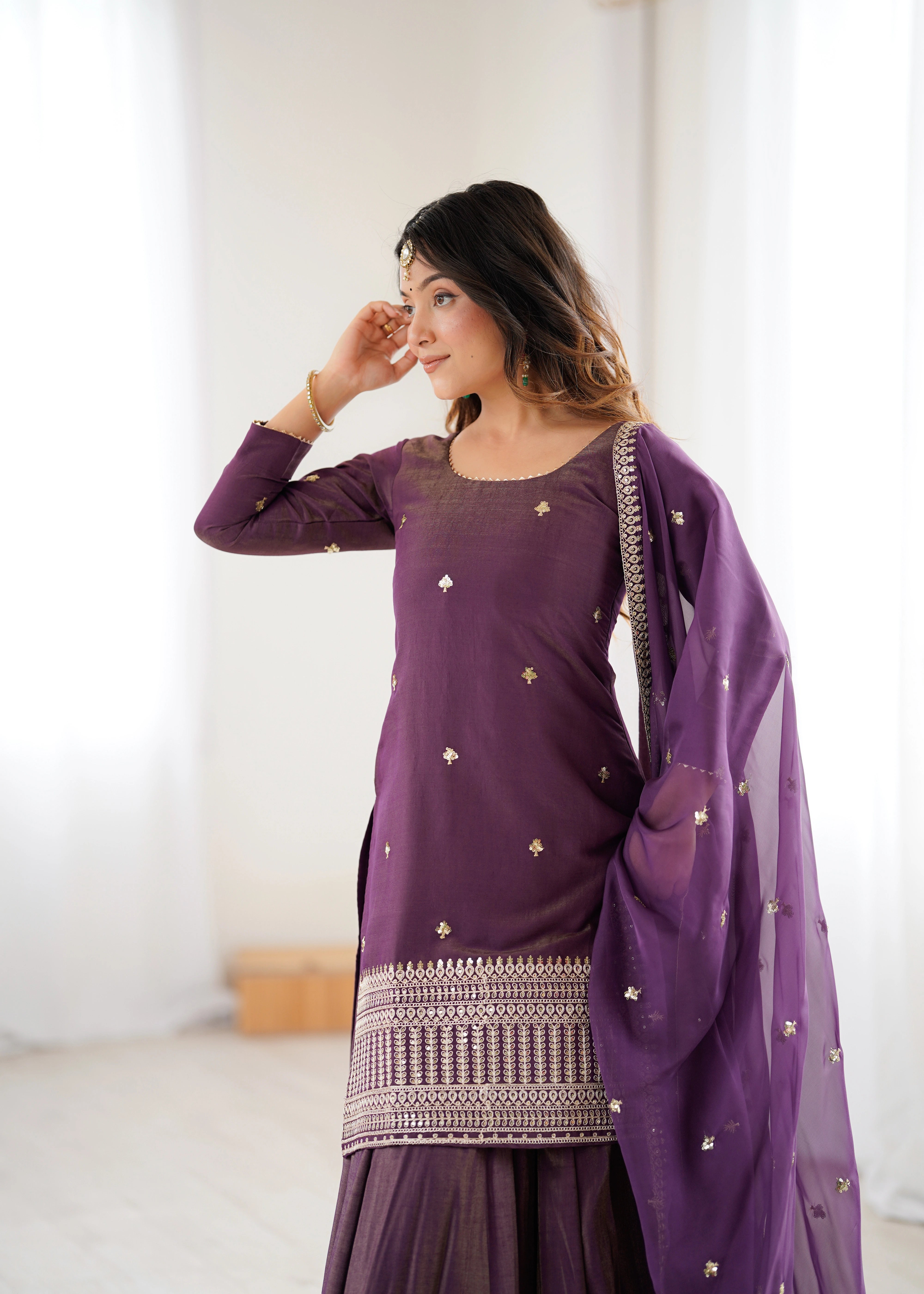 Woman wearing a purple traditional outfit with a matching dupatta indoors.