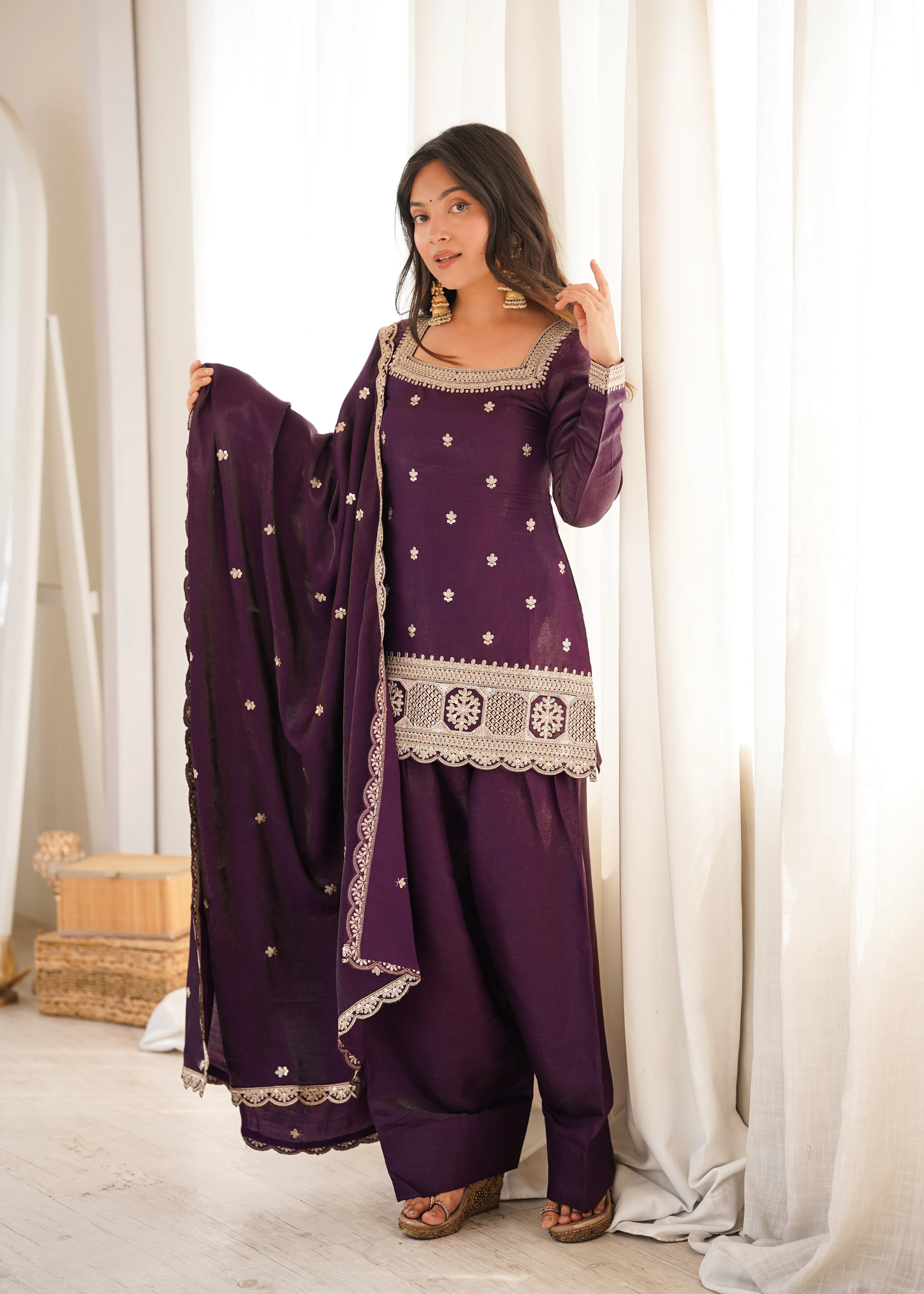Woman wearing a purple traditional outfit with white patterns in a bright room.