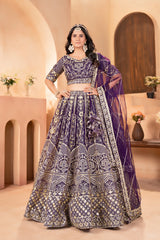 Woman in a traditional purple and silver embroidered outfit standing in an elegant indoor setting.
