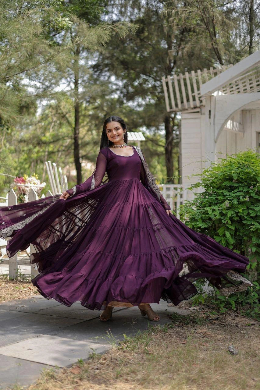 Woman in a long purple dress standing outdoors with trees and a house in the background