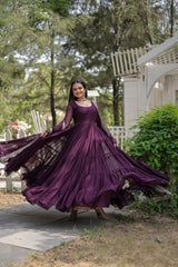 Woman in a long purple dress standing outdoors with trees and a house in the background