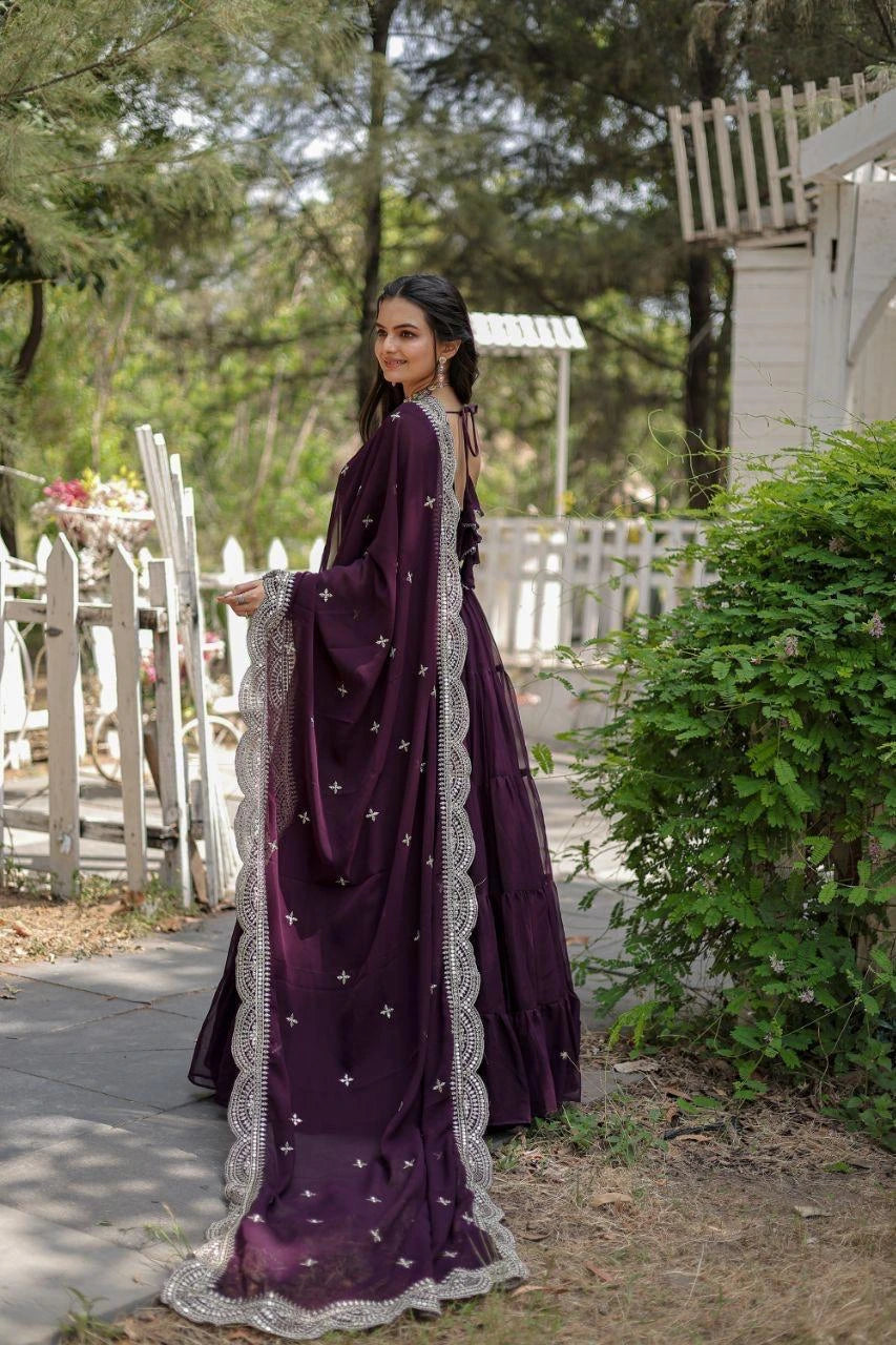 Woman in a purple saree with white lace details standing outdoors.