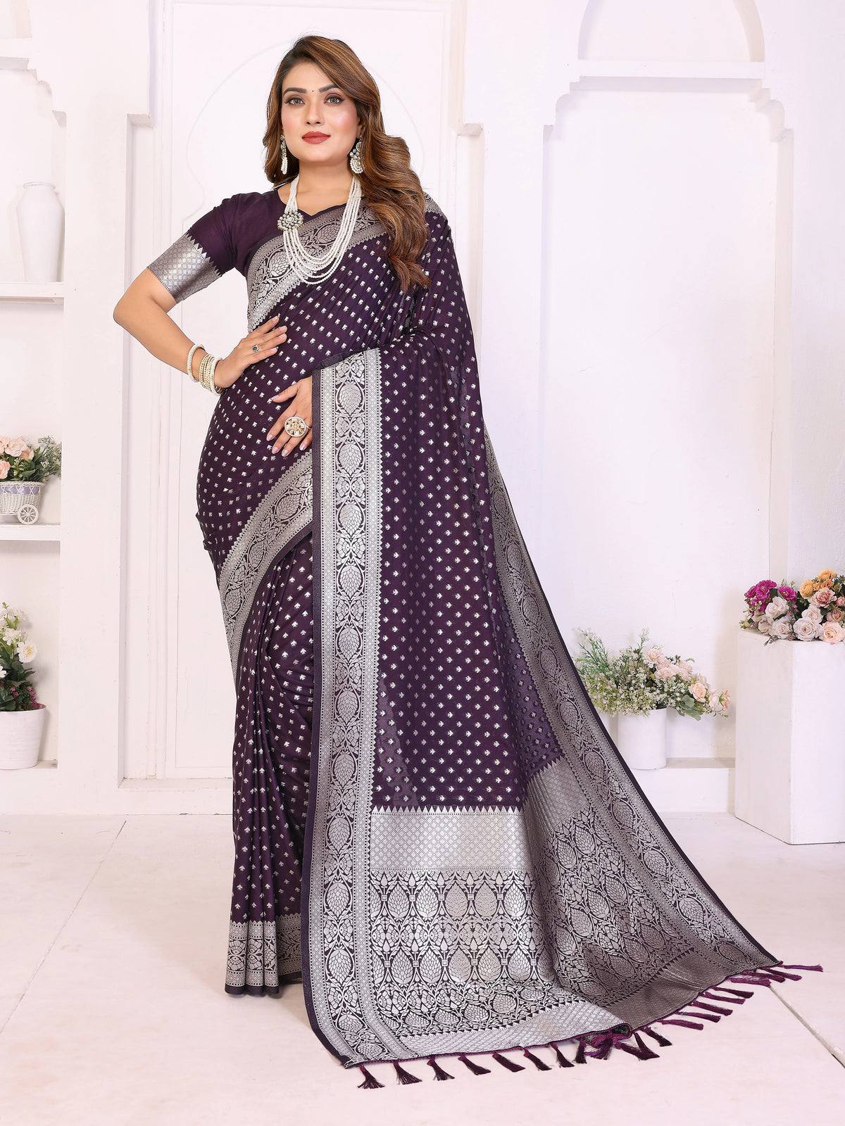 Woman wearing a purple saree with a white and gray border in a white room.
