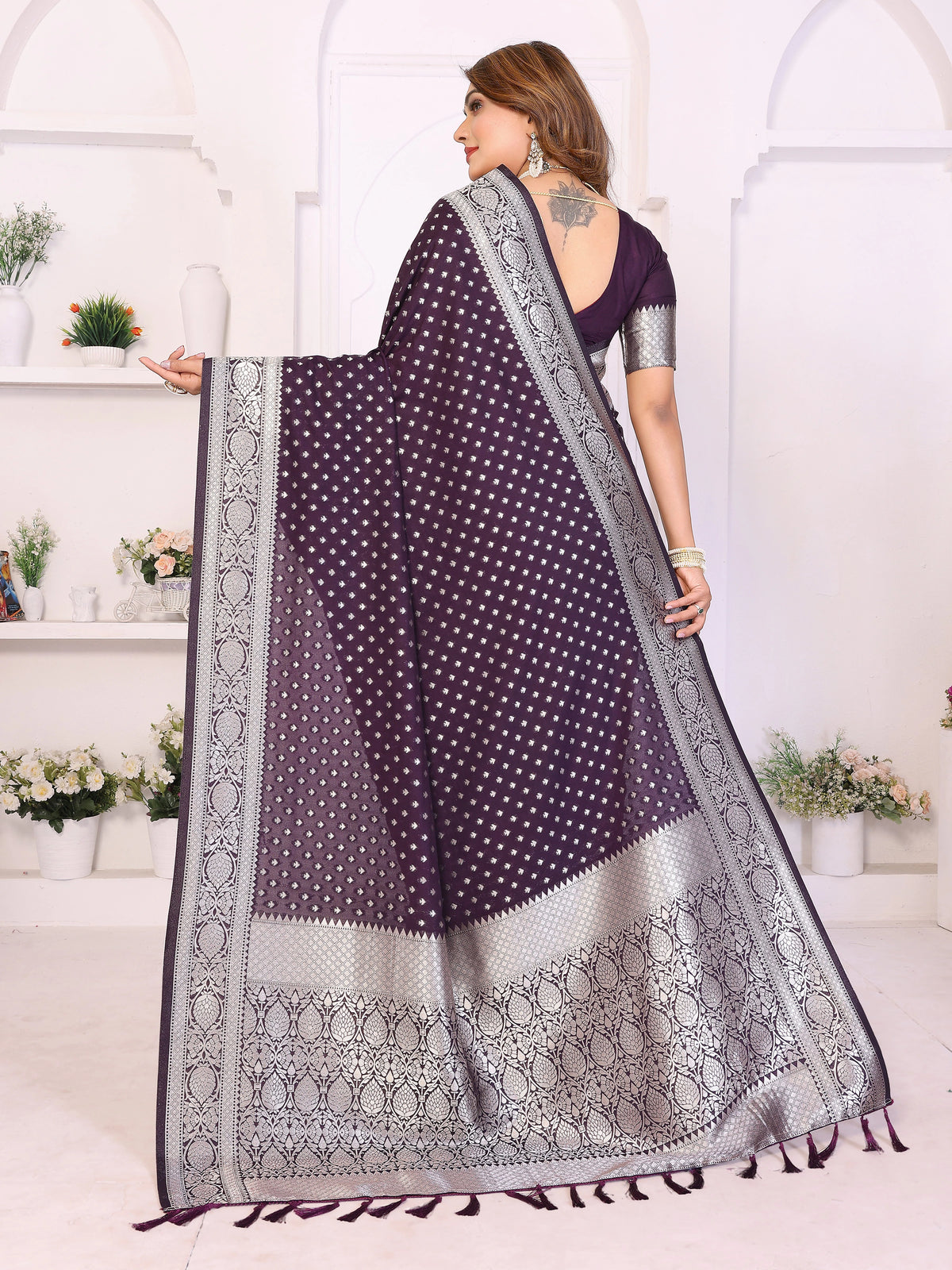 Woman wearing a purple saree with white patterns in a well-lit room.