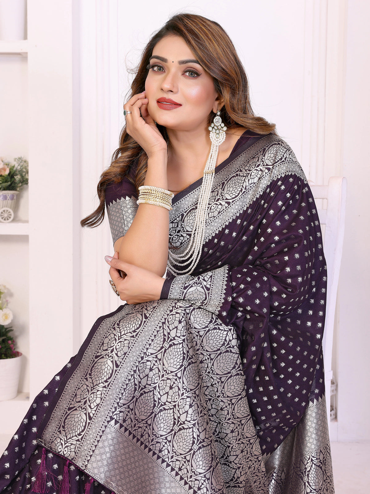 Woman wearing a purple and gray patterned saree with jewelry against a white background
