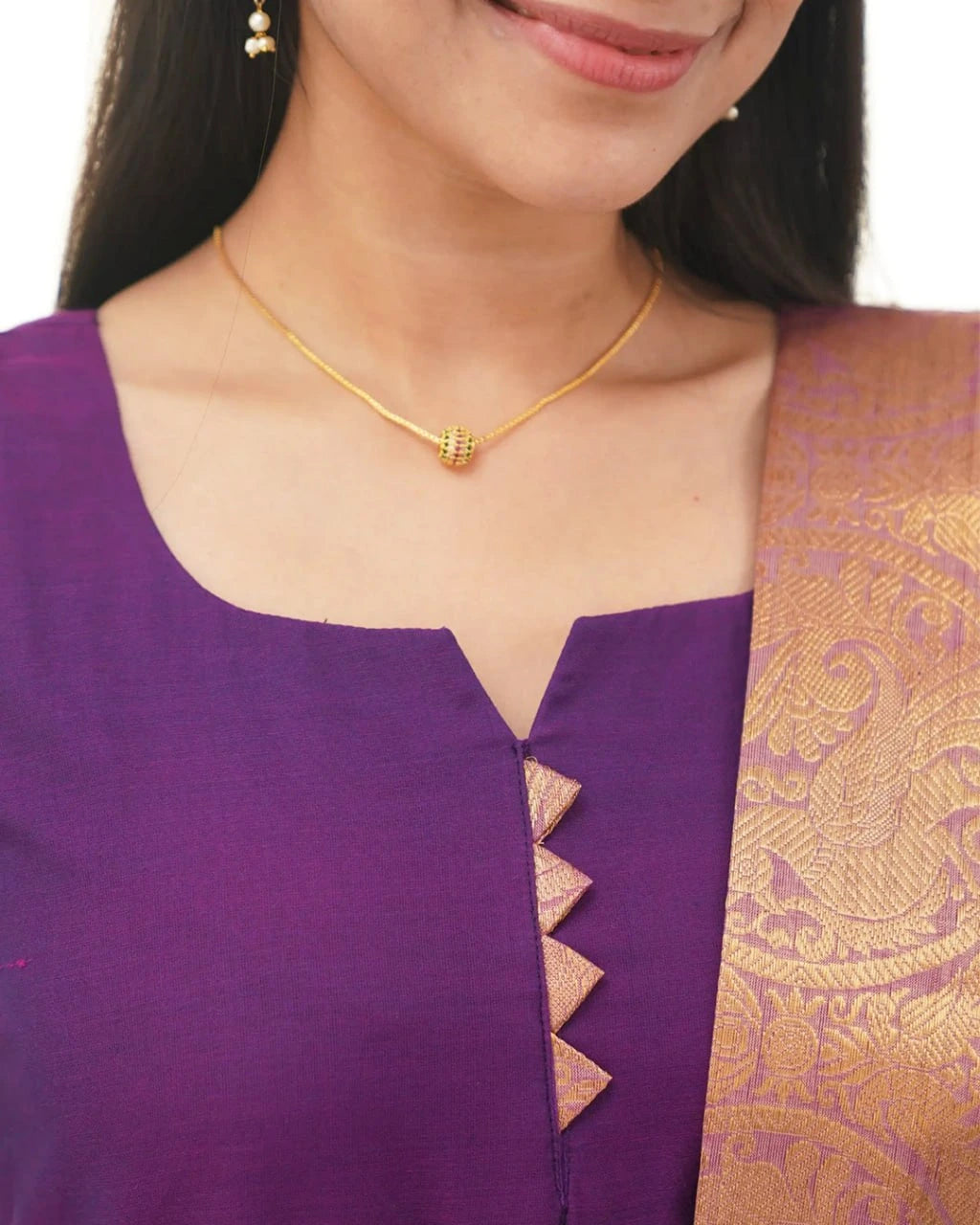 Woman wearing a purple saree with gold border and gold necklace