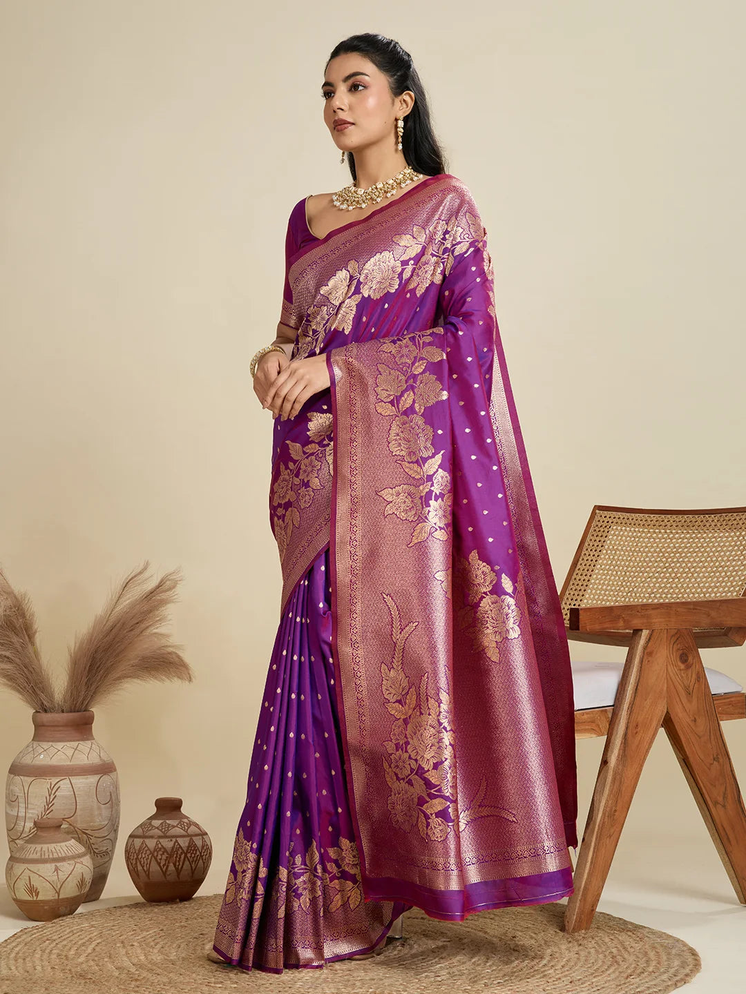 Woman wearing a purple saree with gold patterns in a minimalistic setting.