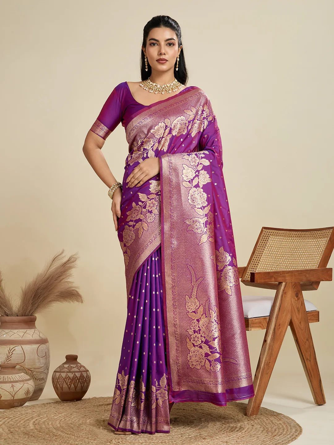 Woman wearing a purple saree with gold patterns in a minimalistic setting.
