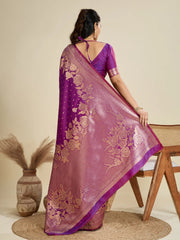 Woman wearing a pink saree with purple border, sitting on a chair against a beige background.