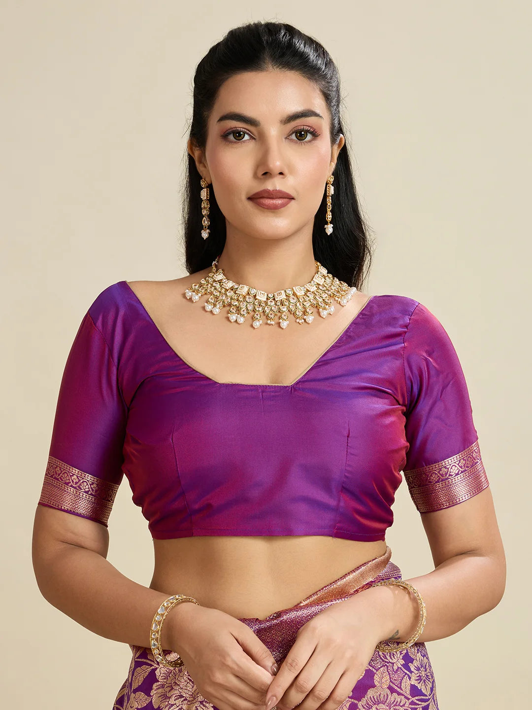Woman wearing a purple blouse with gold details on a beige background