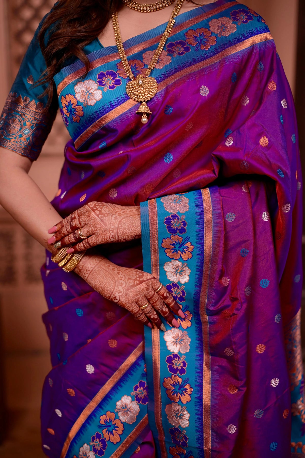 Woman wearing a vibrant purple and blue saree with floral patterns, holding hands together.