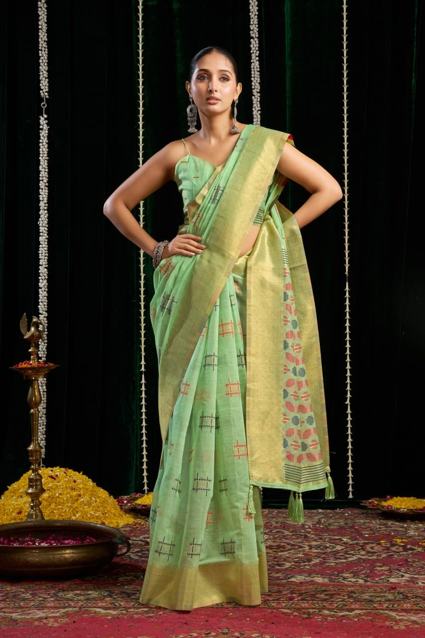 Woman in a green saree with a patterned border standing on a red carpet with decorative elements.