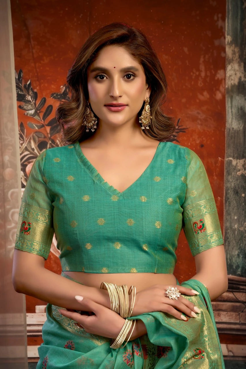 Woman wearing a green saree with gold patterns against a textured wall.