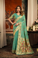Woman wearing a teal saree with floral patterns in an indoor setting.