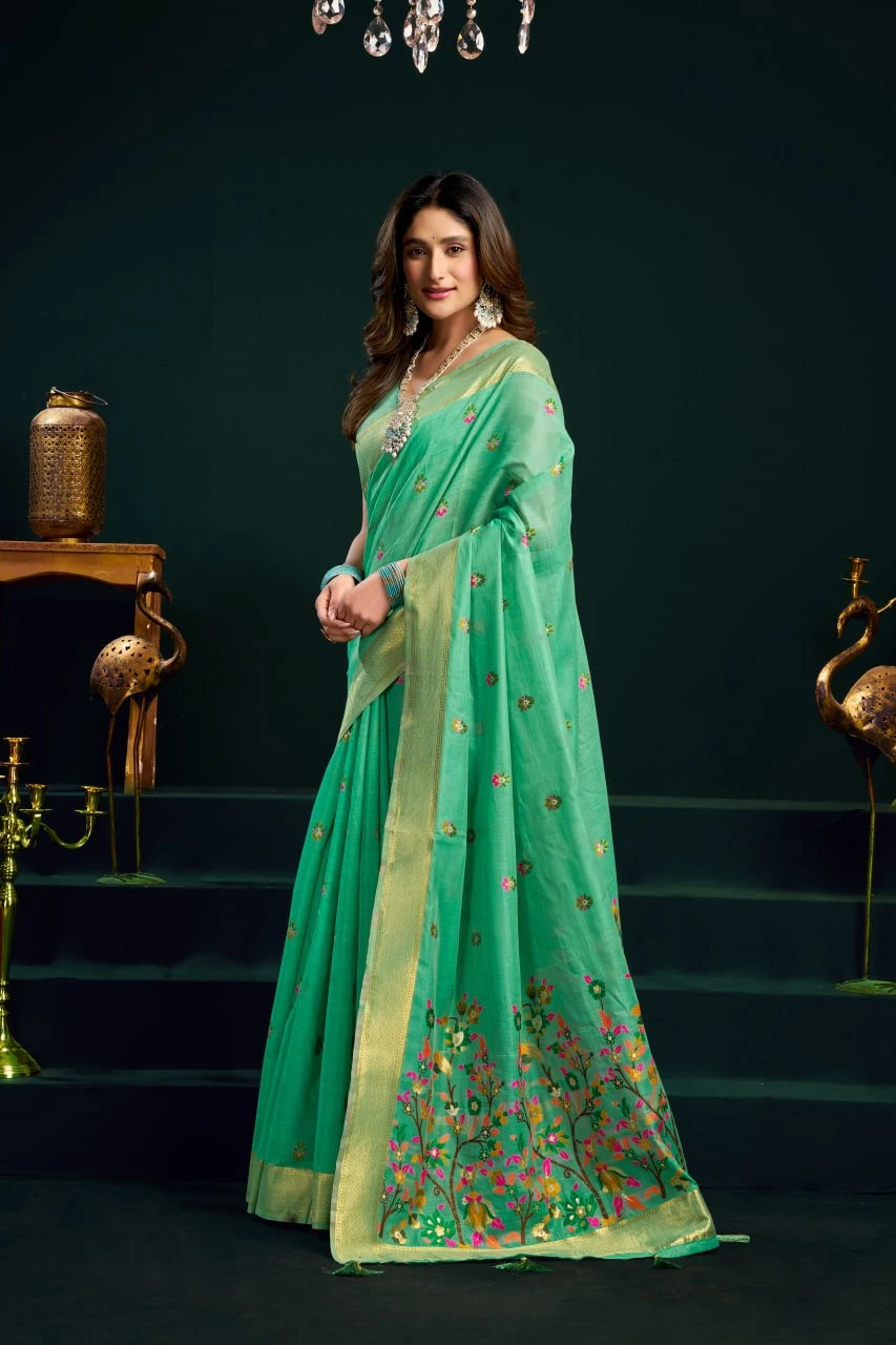 Woman in a green saree with floral patterns standing against a dark background
