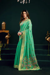 Woman in a green saree with floral patterns standing against a dark background