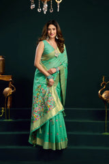 Woman in a green saree with floral patterns standing on steps against a dark background