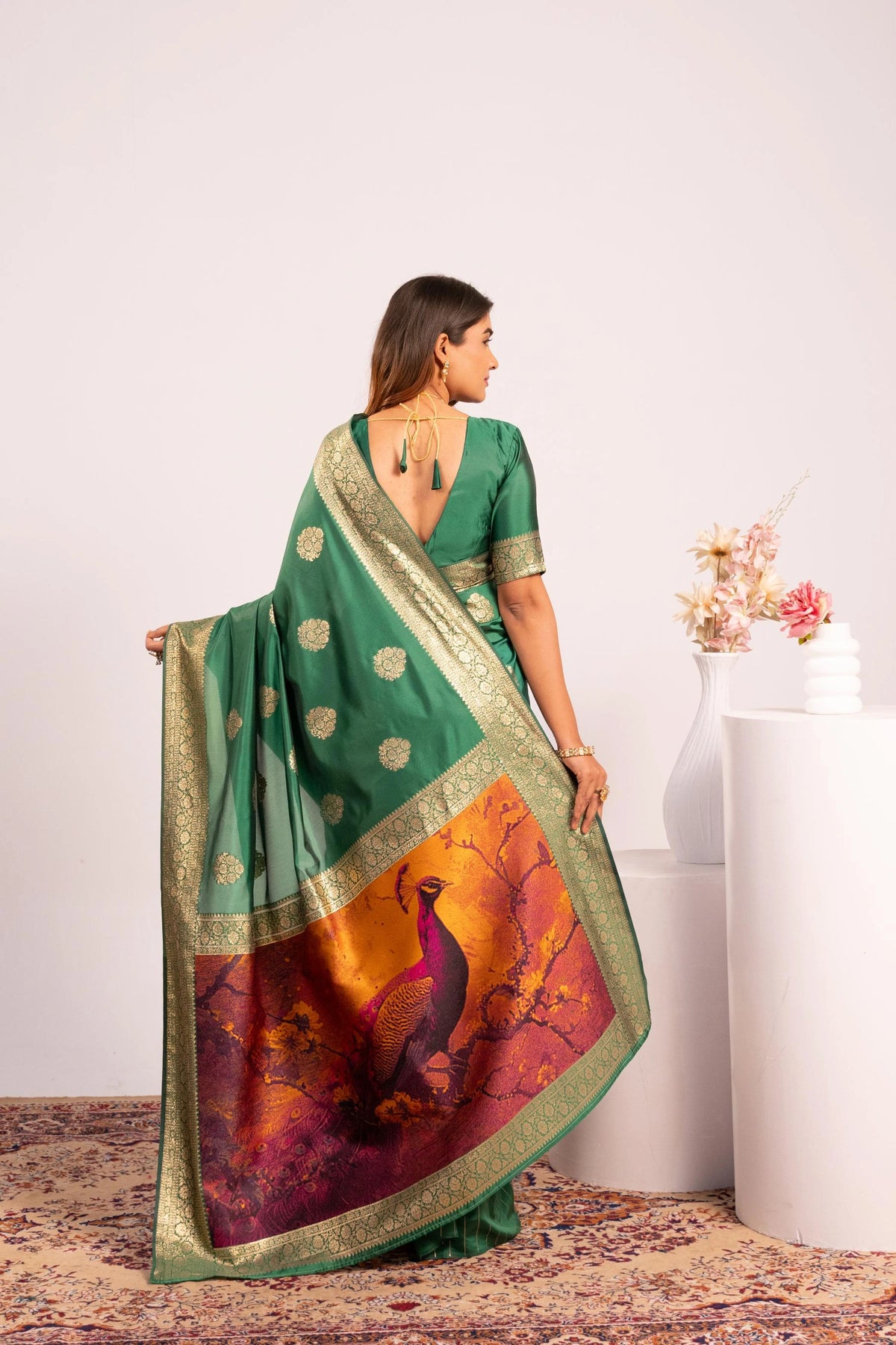 Woman wearing a green saree with a peacock design, standing against a white background.