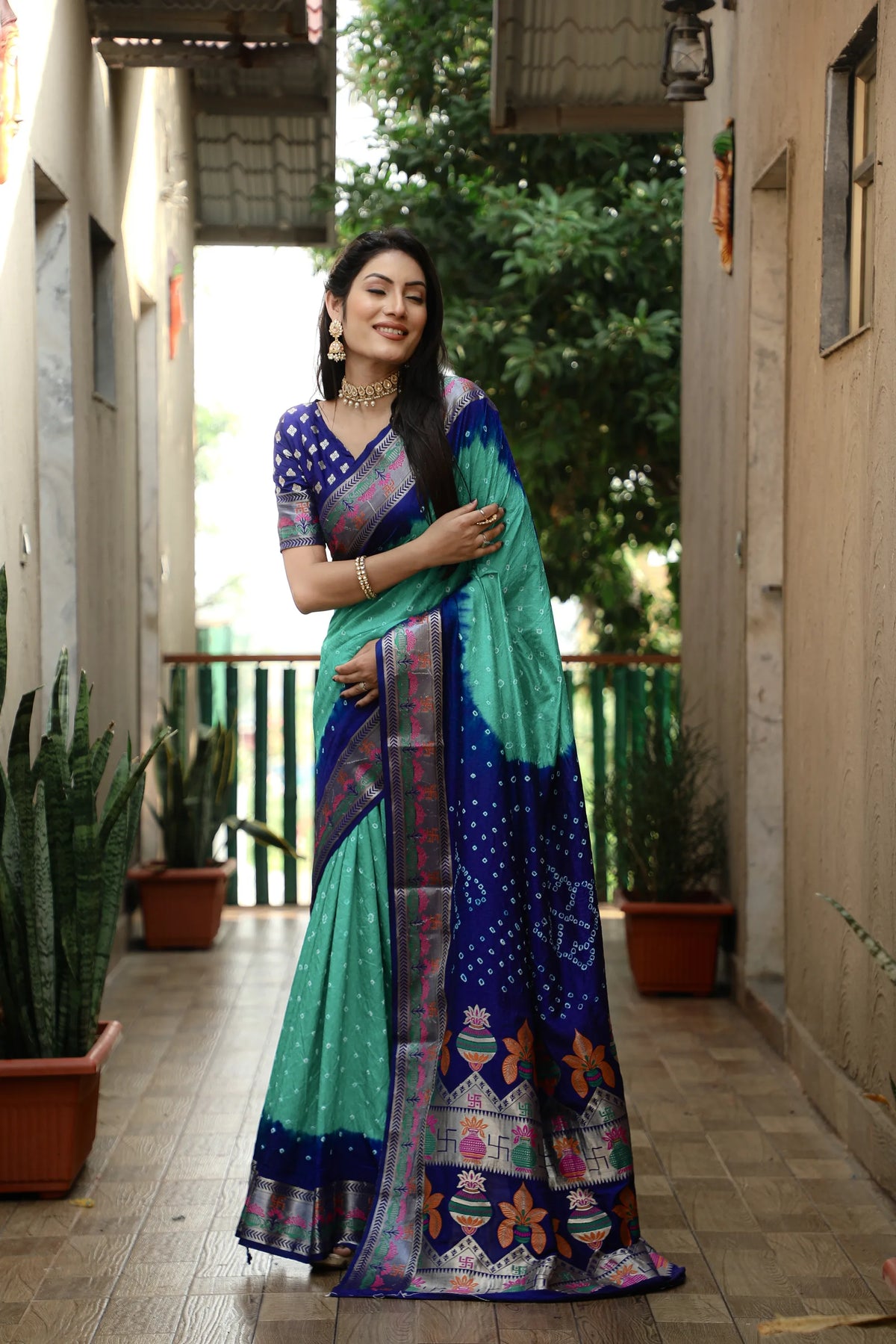 Woman in a colorful saree standing in a corridor with plants.