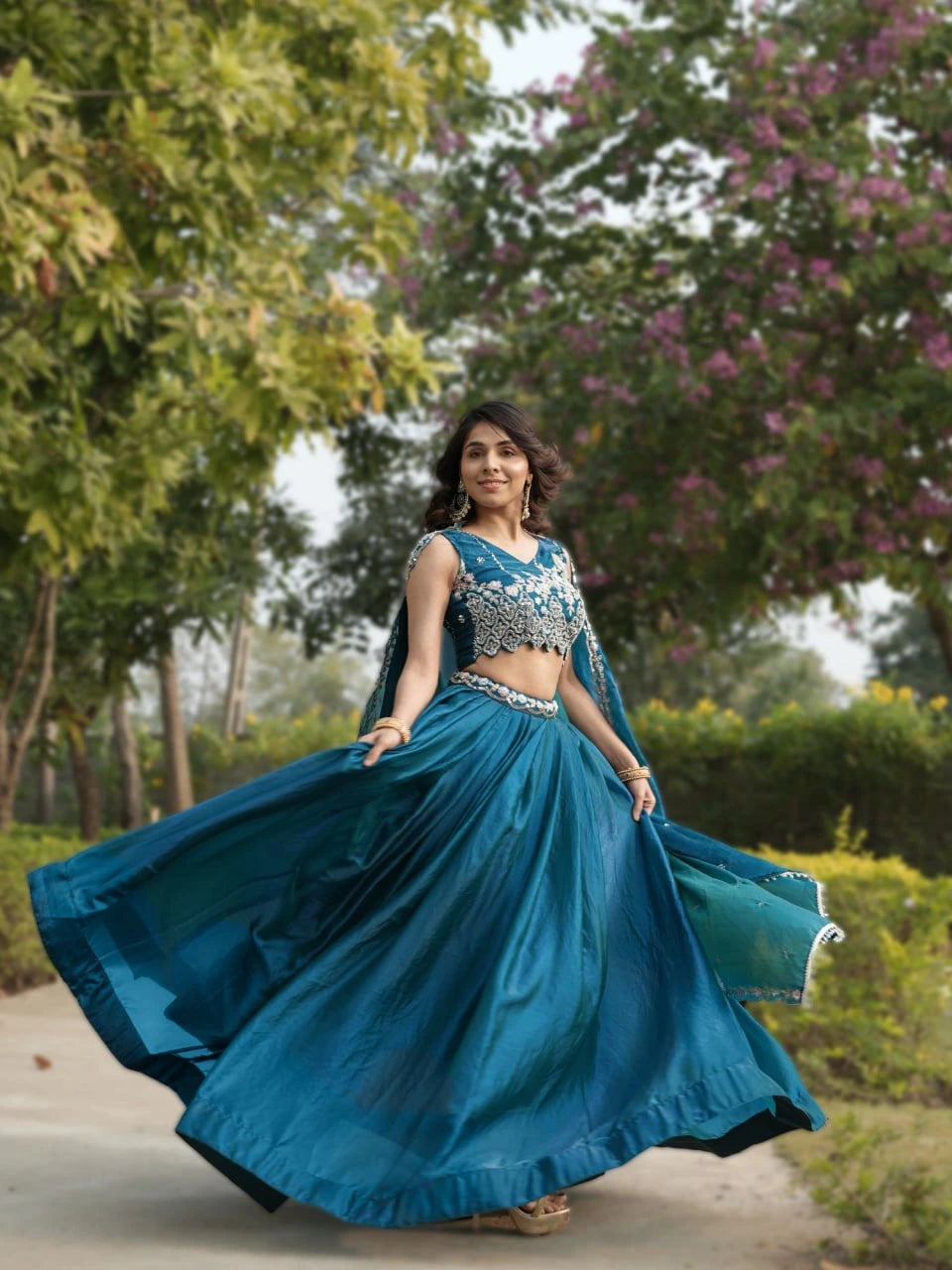 Woman in a blue traditional outfit standing outdoors with greenery in the background