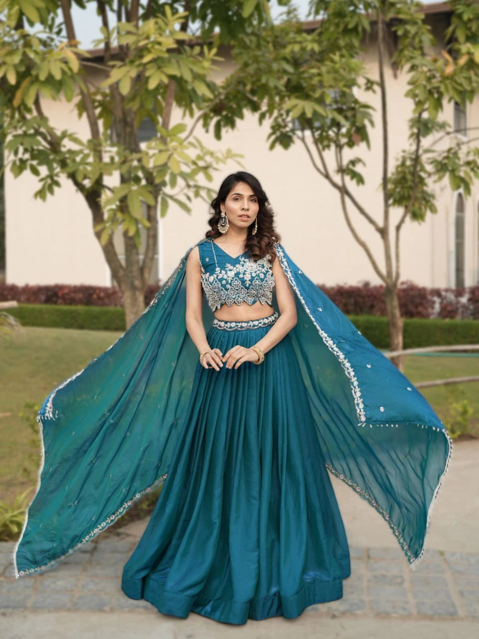 Woman in a teal traditional outfit with a flowing saree in an outdoor setting.