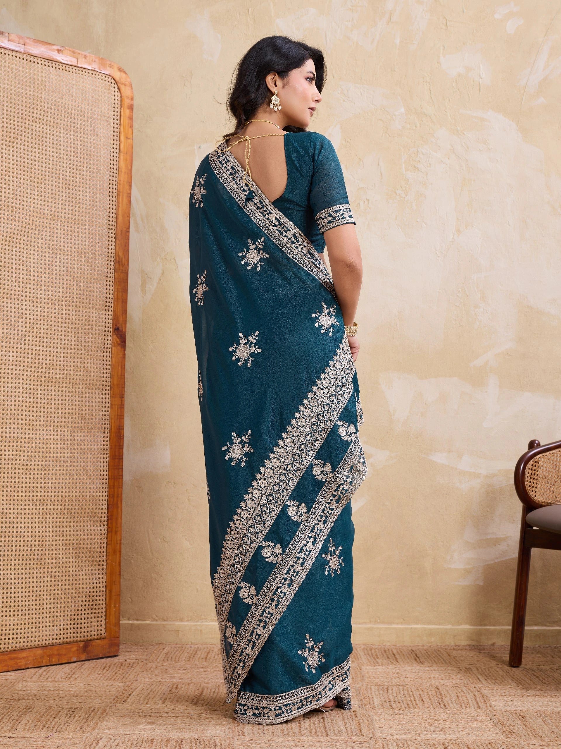 Woman wearing a teal saree with white embroidery in a room setting.