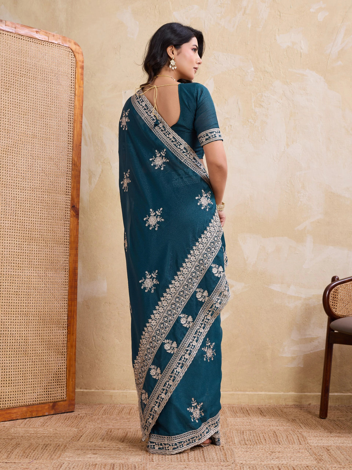 Woman wearing a teal saree with white embroidery in a room setting.