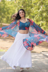 Woman in a blue floral top and white skirt with a colorful shawl outdoors.