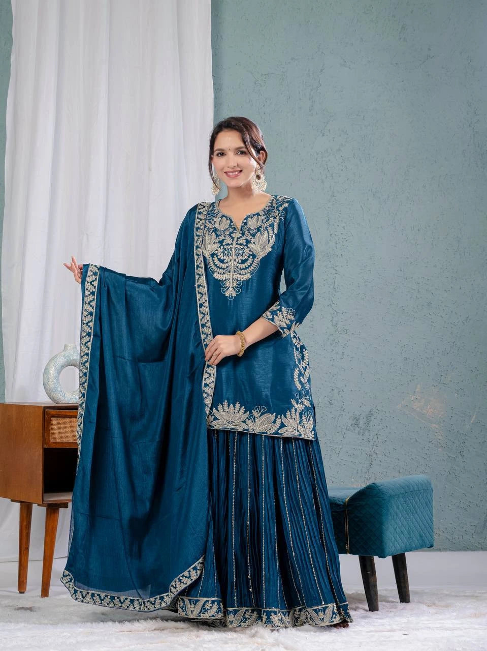 Woman in a blue traditional outfit with silver embroidery standing in a room.