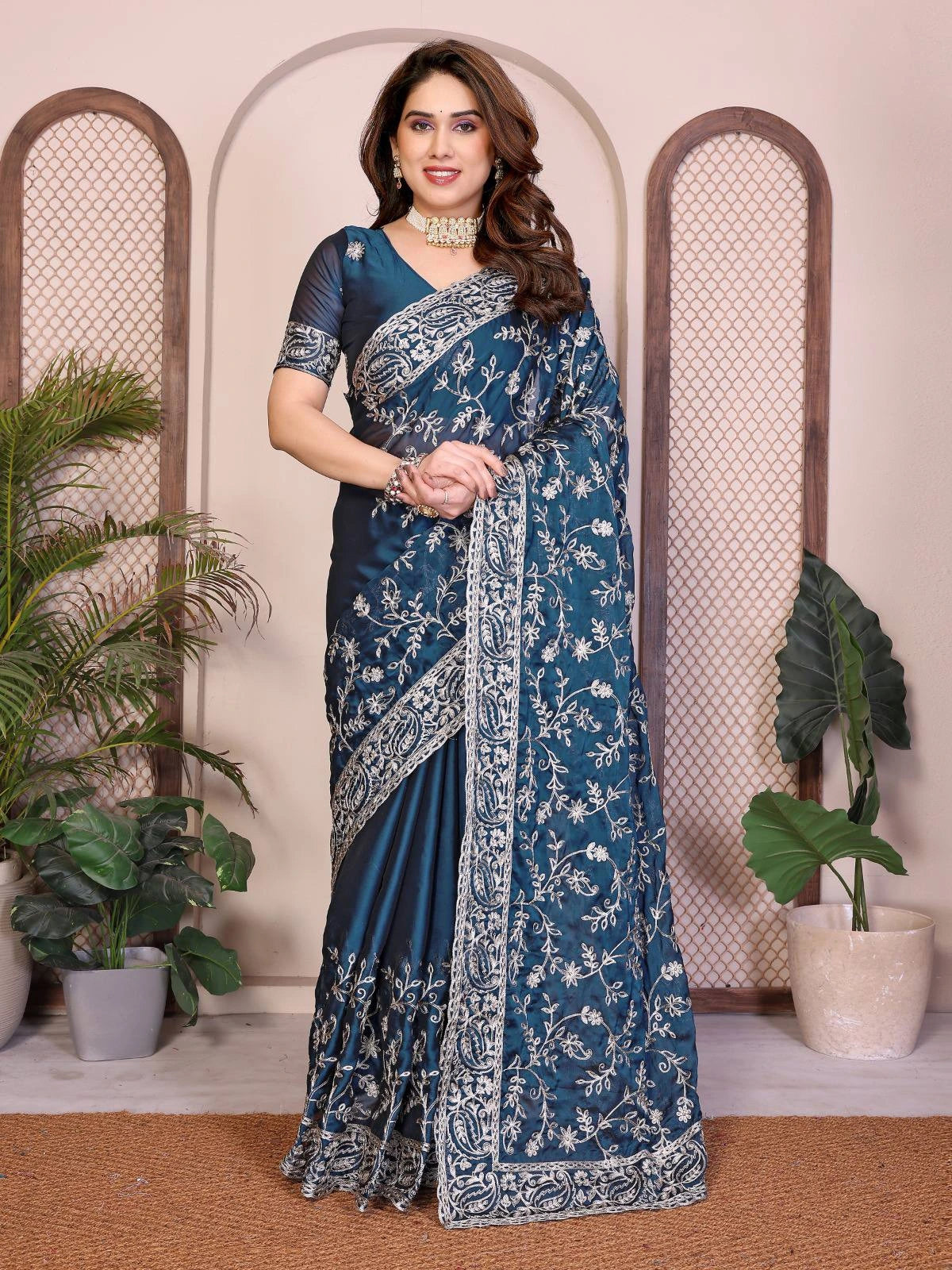 Woman wearing a blue saree with white patterns in a decorative setting with plants.