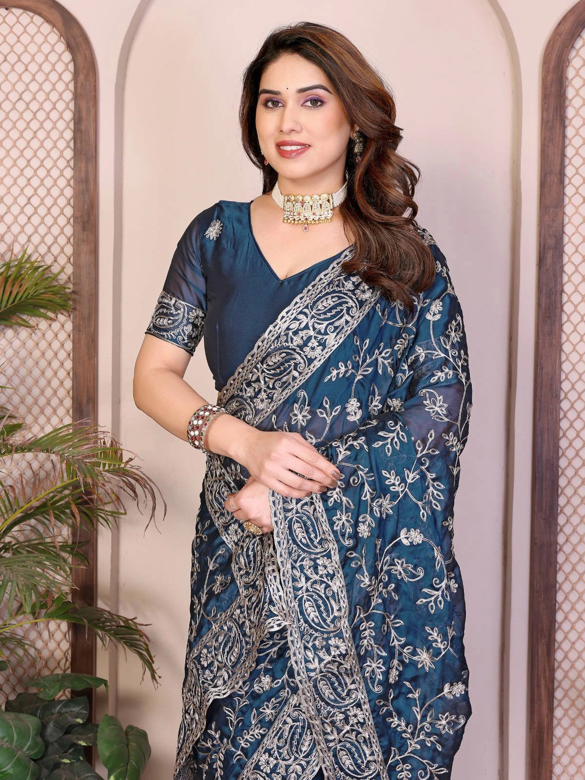 Woman wearing a blue saree with a floral pattern against a neutral background