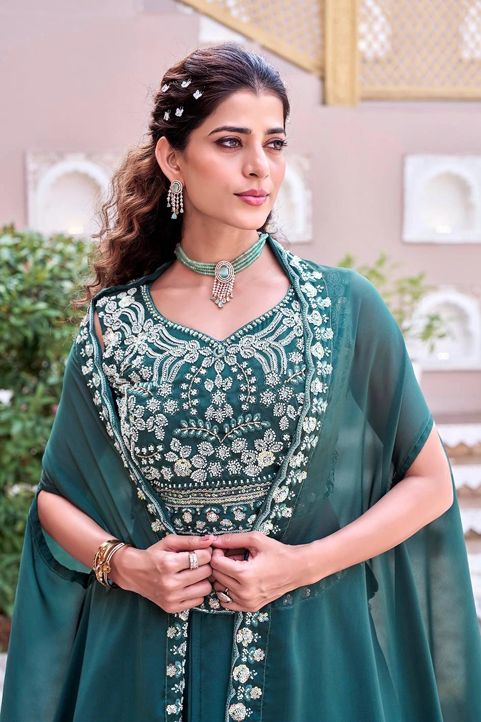 Woman wearing a green embroidered outfit with jewelry in an indoor setting