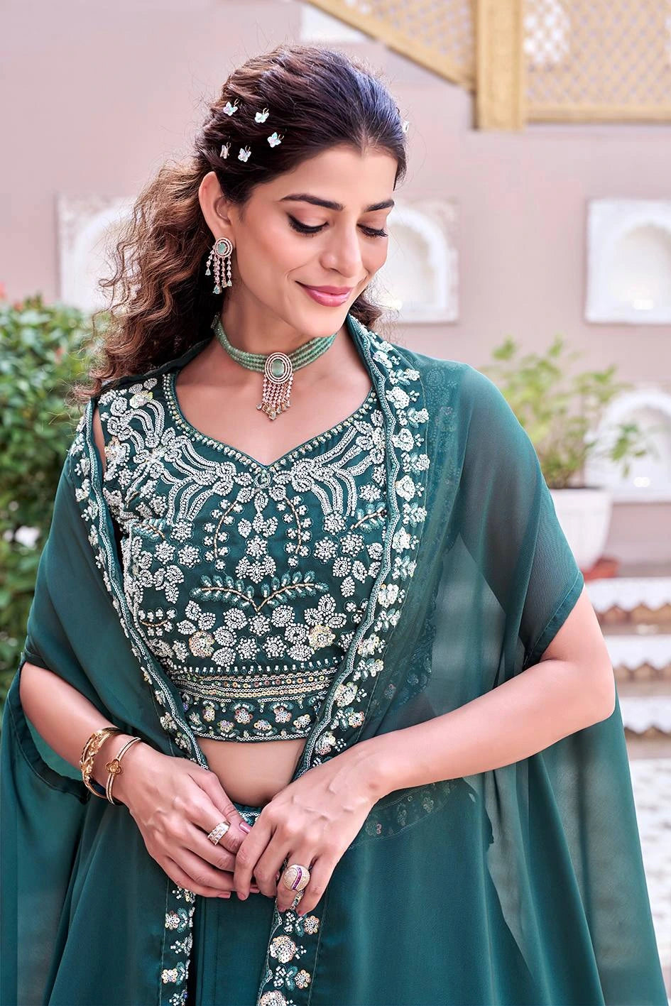 Woman in a green traditional outfit with intricate designs, standing indoors.