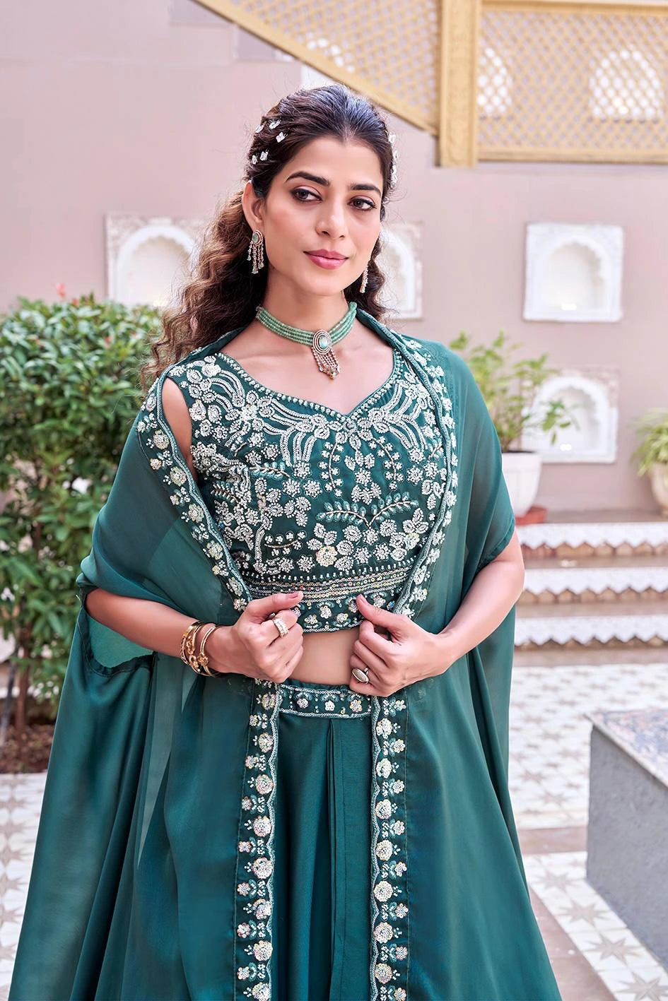 Woman in a green traditional outfit with intricate designs, standing outdoors.
