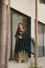 Woman in a dark green traditional outfit with gold details standing in front of a modern building.