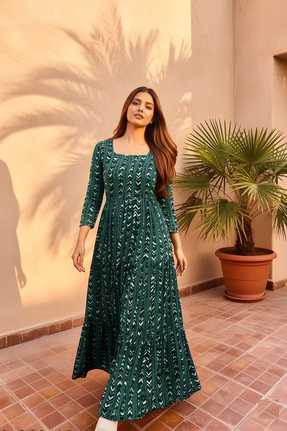 Woman in a green dress standing in front of a palm tree and a wall with a plant.