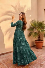 Woman in a green dress standing in a sunlit room with a plant in the background