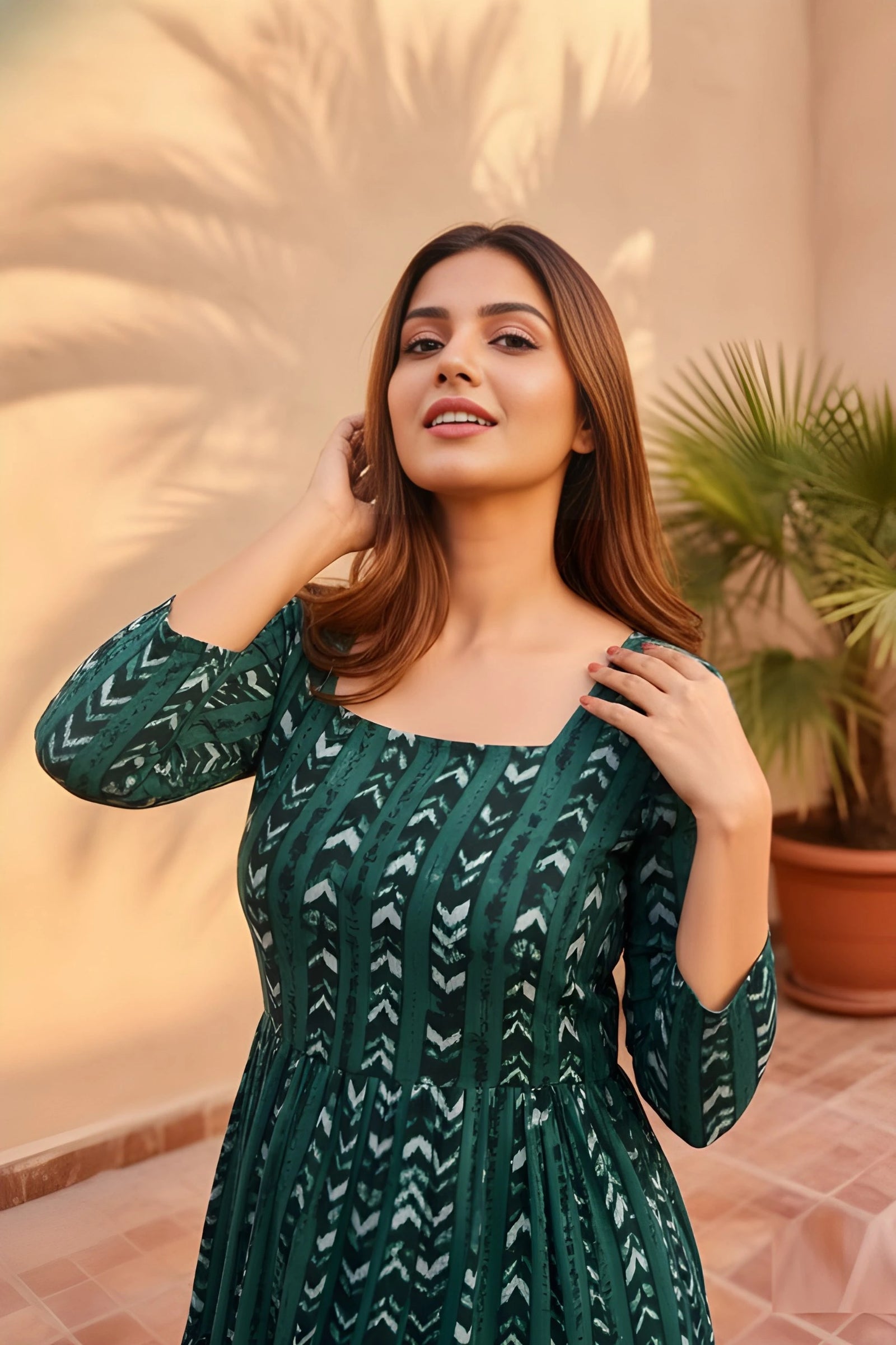 Woman wearing a green patterned dress standing outdoors with plants in the background