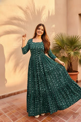 Woman in a long green dress standing outdoors with a plant in the background