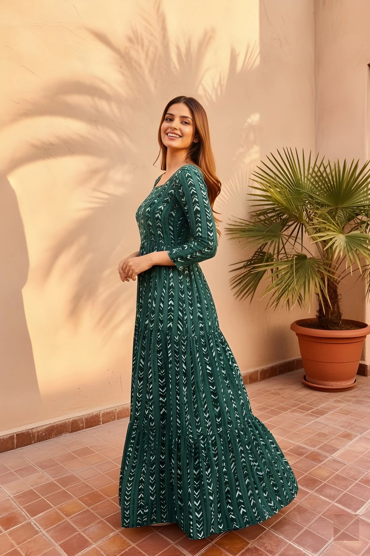 Woman in a green dress standing in front of a textured wall with a plant.